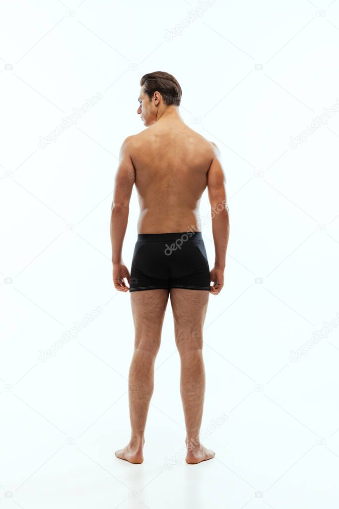 Back view of young handsome shirtless sportive man wearing black boxer-briefs standing isolated on white studio background.