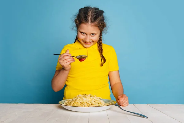 Cute little girl, emotive kid eating delicious Italian pasta isolated on blue studio background. World pasta day — Stockfoto