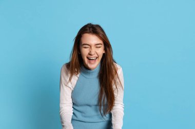 Mavi stüdyo arka planında, uzun parlak saçlı, gülen güzel bir kızın yarım boy portresi. İnsani duygular, yüz ifadesi kavramı