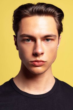 Yakından genç yakışıklı bir adam sarı stüdyo arka planında izole edilmiş. İyi korunmuş derisi ve hafif kılları olan bir model.