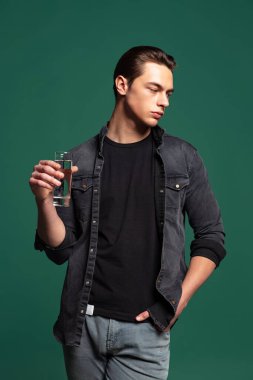 Siyah tişört ve ekose gömlek giyen yakışıklı bir adamın stüdyo resmi. Yeşil stüdyo arka planında tek başına duran kot pantolon..
