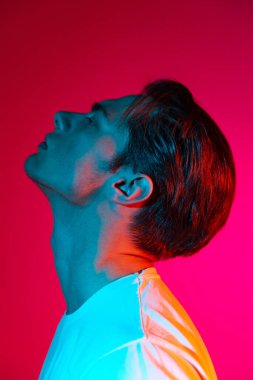 Genç, ciddi bir adam, eflatun renkli stüdyo arka planında, neon ışıkta, insan duyguları kavramında, yüz ifadesinde yalnız poz veriyor. Yan görünüm