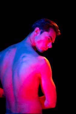 Arkadan bak. Genç adam portresi, karanlık stüdyo arka planında pembe neonlarla izole edilmiş, insan duyguları kavramı, yüz ifadesi.