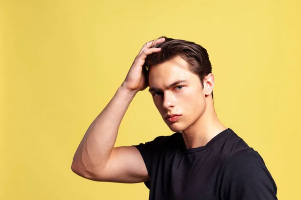Close-up portret młodego przystojnego mięśniaka w czarnym t-shirt patrząc na aparat odizolowany na żółtym tle studio. — Zdjęcie stockowe
