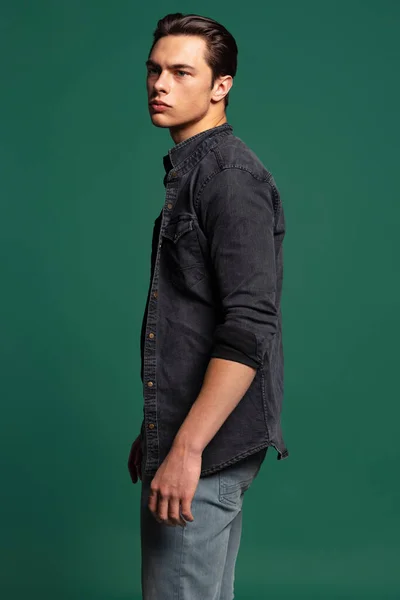 Studioaufnahme eines jungen, gut aussehenden, sportlichen Mannes mit schwarzem T-Shirt und kariertem Hemd, Jeans isoliert auf grünem Studiohintergrund. — Stockfoto