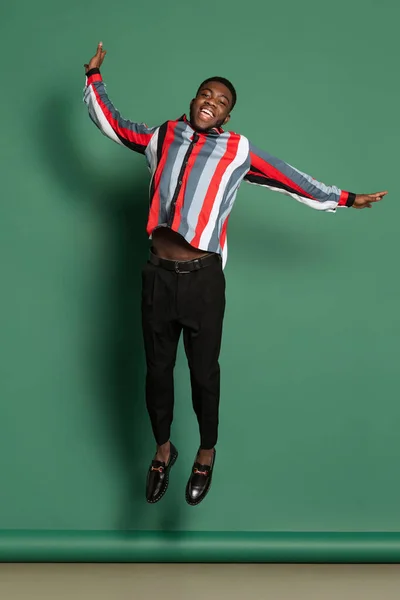 Studio shot of african man in bright shirt jumping isolated over dark green color background. Wow emotions concept — Fotografia de Stock