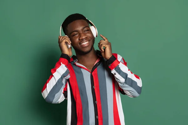 Portret van jonge gelukkige Afrikaanse man die luistert naar muziek geïsoleerd op groene studio achtergrond met copyspace voor advertentie. — Stockfoto