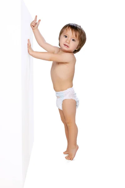 Porträtt av liten pojke, baby, barn i blöja står nära väggen isolerad över vit studio bakgrund. Begreppet barndom — Stockfoto