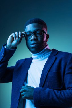 Beyaz yaka polo ve ceket giyen genç Afrikalı bir adamın mavi arka planda izole edilmiş yarım boy portresi..