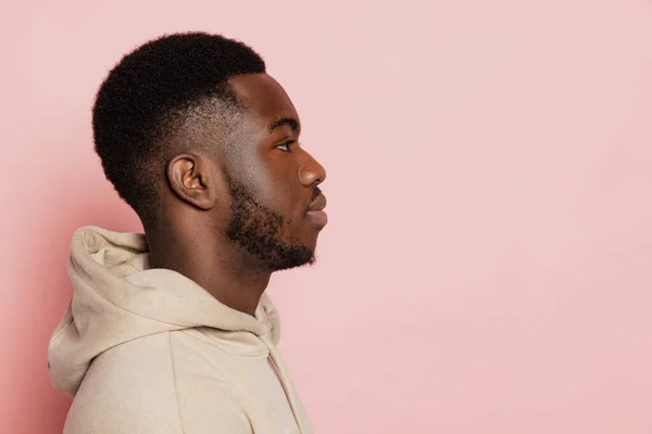 Профиль взгляд молодого серьезного темнокожего человека смотрит прямо перед собой изолирован на розовом фоне студии с копирайтом для рекламы. — стоковое фото
