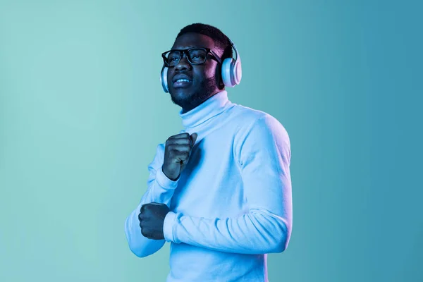 Studio shot van jonge modieuze jongen, student met witte nek-polo en jeans geïsoleerd op blauwe achtergrond in neon licht. — Stockfoto