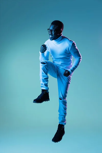Studio ditembak pemuda modis, siswa mengenakan polo leher putih dan celana jeans terisolasi di latar belakang biru dalam cahaya neon. — Stok Foto