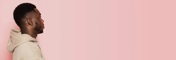 Perfil de jovem sério homem de pele escura olha em frente isolado no fundo do estúdio rosa com copyspace para anúncio. — Fotografia de Stock