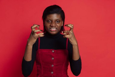 Koyu kırmızı stüdyo arka planında izole edilmiş kızgın, koyu tenli genç bir kız. Duyguların kavramı, yüz ifadeleri