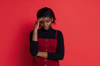 Koyu kırmızı stüdyo geçmişine izole edilmiş üzgün, koyu tenli genç bir kız. Duyguların kavramı, yüz ifadeleri