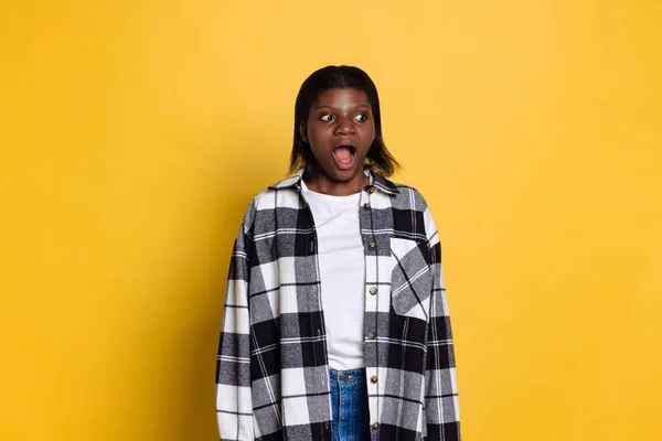 Shocked young beautiful dark skinned girl standing with open mouth isolated on yellow studio background. — Stockfoto