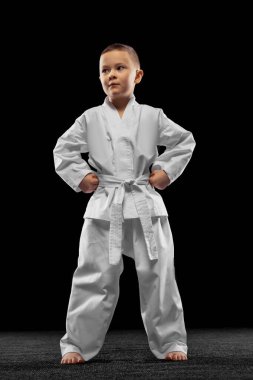 Küçük bir çocuk, çocuk, beyaz dobok giyen tekvando atleti karanlık arka planda izole edilmiş. Spor, eğitim, beceri kavramı