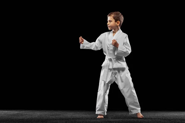 Egy kisfiú, fiú, taekwondo atléta pózol elszigetelve a sötét háttérben. A sport, az oktatás és a készségek fogalma — Stock Fotó