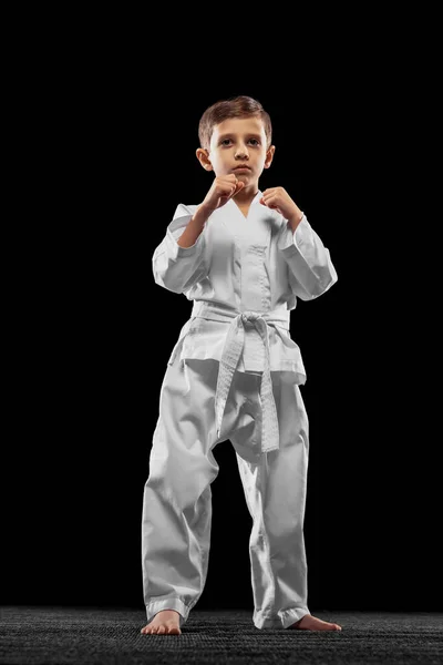 Egy kissrác, fiú, taekwondo atléta fehér dobokot visel, sötét háttérrel elszigetelve. A sport, az oktatás és a készségek fogalma — Stock Fotó