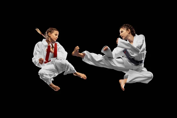 Δύο νεαρά κορίτσια, έφηβοι, αθλητές taekwondo προπονούνται μαζί απομονωμένοι σε σκοτεινό φόντο. Έννοια του αθλητισμού, της εκπαίδευσης, των δεξιοτήτων — Φωτογραφία Αρχείου