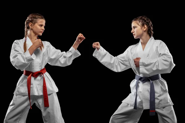 Δύο νεαρά κορίτσια, έφηβοι, αθλητές taekwondo προπονούνται μαζί απομονωμένοι σε σκοτεινό φόντο. Έννοια του αθλητισμού, της εκπαίδευσης, των δεξιοτήτων — Φωτογραφία Αρχείου
