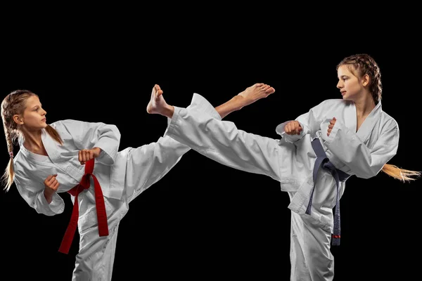 Two young girls, teens, taekwondo athletes training together isolated over dark background. Concept of sport, education, skills — Stock Photo, Image