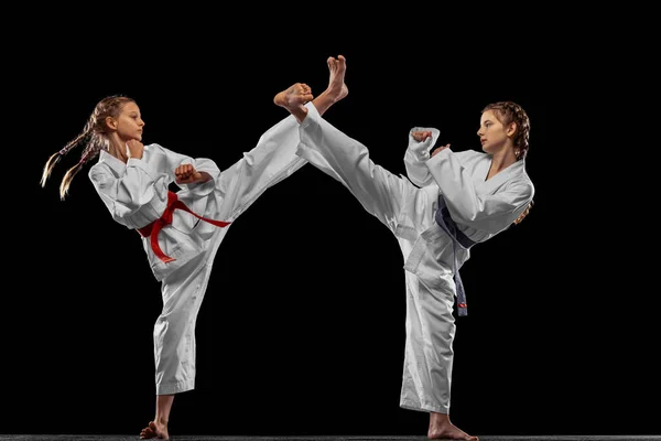 Twee jonge meisjes, tieners, taekwondo atleten trainen samen geïsoleerd over donkere achtergrond. Begrip sport, onderwijs, vaardigheden — Stockfoto