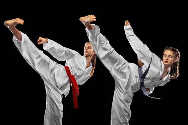 Dos chicas jóvenes, adolescentes, atletas taekwondo entrenando juntas aisladas sobre un fondo oscuro. Concepto de deporte, educación, habilidades — Foto de Stock