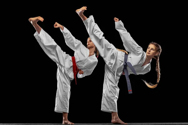 Két fiatal lány, tizenévesek, taekwondo sportolók edzés együtt elszigetelt sötét háttérrel. A sport, az oktatás és a készségek fogalma — Stock Fotó