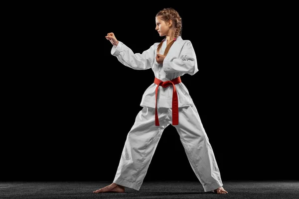 One young girl, teen, taekwondo athlete posing isolated over dark background. Concept of sport, education, skills — Stock Photo, Image