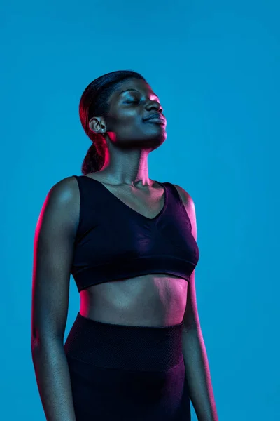 Portrait of young beautiful dark skinned woman posing isolated on blue studio background in neon light. — стоковое фото