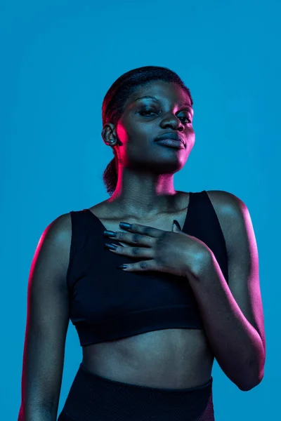 Porträt einer jungen schönen dunkelhäutigen Frau, die isoliert auf blauem Studiohintergrund im Neonlicht posiert. — Stockfoto