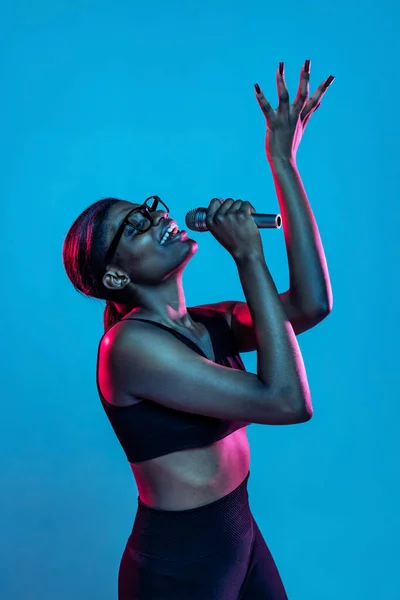 Porträt einer jungen schönen dunkelhäutigen Frau, die isoliert auf blauem Studiohintergrund im Neonlicht posiert. — Stockfoto