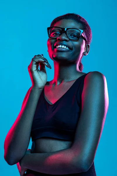 Nahaufnahme Porträt einer jungen schönen dunkelhäutigen Frau, die isoliert auf blauem Studiohintergrund im Neonlicht posiert. — Stockfoto