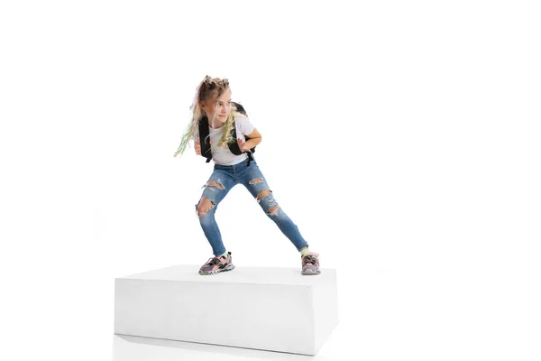 Full-length portrait of smiling girl in casual clothes standing on big box isolated on white studio background. Happy childhood concept. — Stock Photo, Image