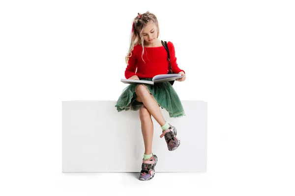 One beautiful little cute girl in casual clothes sitting on big box isolated on white studio background. Happy childhood concept. — Fotografia de Stock