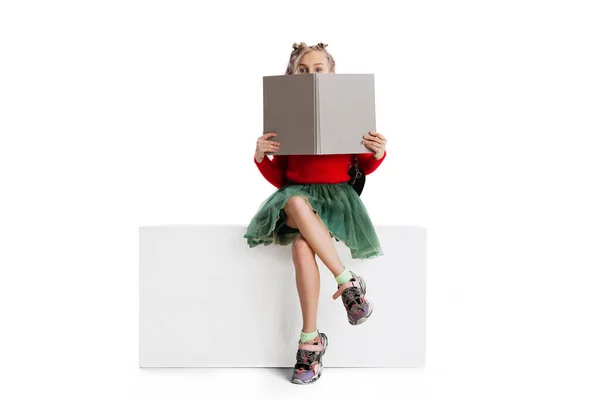 一个穿着休闲装的漂亮可爱小女孩坐在一个大盒子上，与白色的工作室背景隔离。快乐童年的概念. — 图库照片