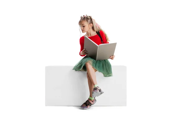 一个穿着休闲装的漂亮可爱小女孩坐在一个大盒子上，与白色的工作室背景隔离。快乐童年的概念. — 图库照片