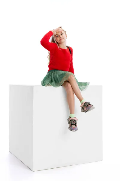 One beautiful little cute girl in casual clothes sitting on big box isolated on white studio background. Happy childhood concept. — Fotografia de Stock