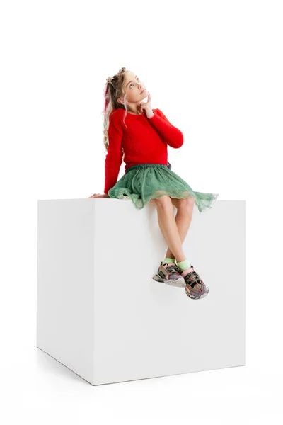 One beautiful little cute girl in casual clothes sitting on big box isolated on white studio background. Happy childhood concept. — Fotografia de Stock
