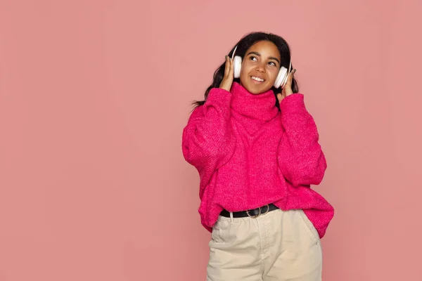 Half-length portrait of young pretty dark skinned girl in warm knitted sweater isolated on pink background. — Stock Photo, Image