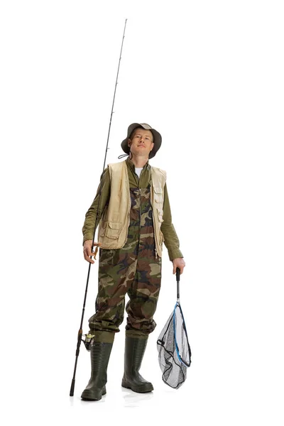 Portrait of young man, professional fisherman with fishing rod, spinning and equipment going to river isolated over white studio background — Stockfoto