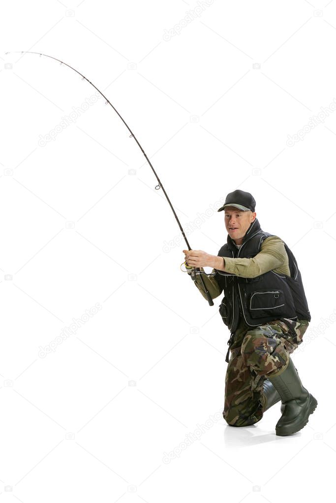 Portrait of young man, professional fisherman with fishing rod, spinning and equipment going to river isolated over white studio background