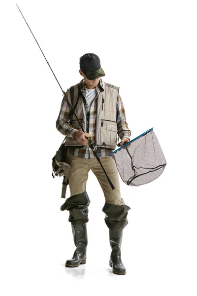 Portrait of young man, professional fisherman with fishing rod, spinning and equipment going to river isolated over white studio background — Stock Photo, Image