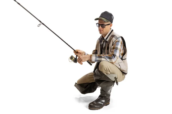 Portrait of young man, professional fisherman with fishing rod, spinning and equipment going to river isolated over white studio background — Stock Photo, Image