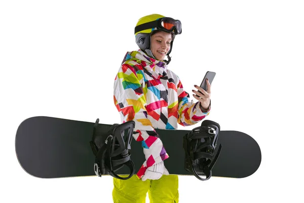 Gelukkig jong meisje in heldere sportkleding, bril en helm staan met snowboard geïsoleerd op witte studio achtergrond. Begrip wintersport — Stockfoto