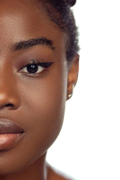 De cerca. La mitad de la cara de la joven mujer africana con la piel bien cuidada aislada en el fondo del estudio blanco. Detalles. —  Fotos de Stock