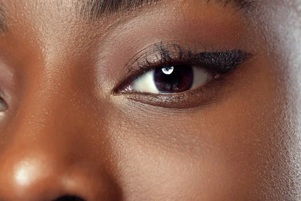 Gros plan sur le visage d'une jeune femme africaine à la peau bien entretenue, isolée sur fond sombre de studio. Détails. — Photo