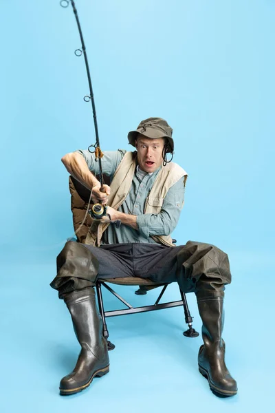Genç bir adamın portresi, balıkçı oltası, dönen ve ekipman mavi stüdyo arka planında izole bir şekilde duruyor. — Stok fotoğraf