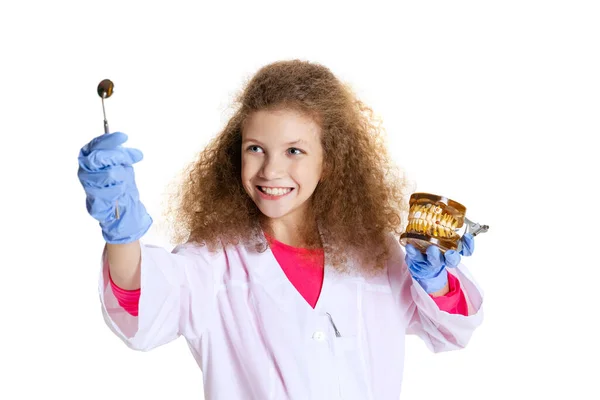 Fröhliche niedliche rothaarige Mädchen, Kind in Bild des Zahnarztes Arzt trägt weißen Labormantel und Handschuhe isoliert auf weißem Studiohintergrund — Stockfoto